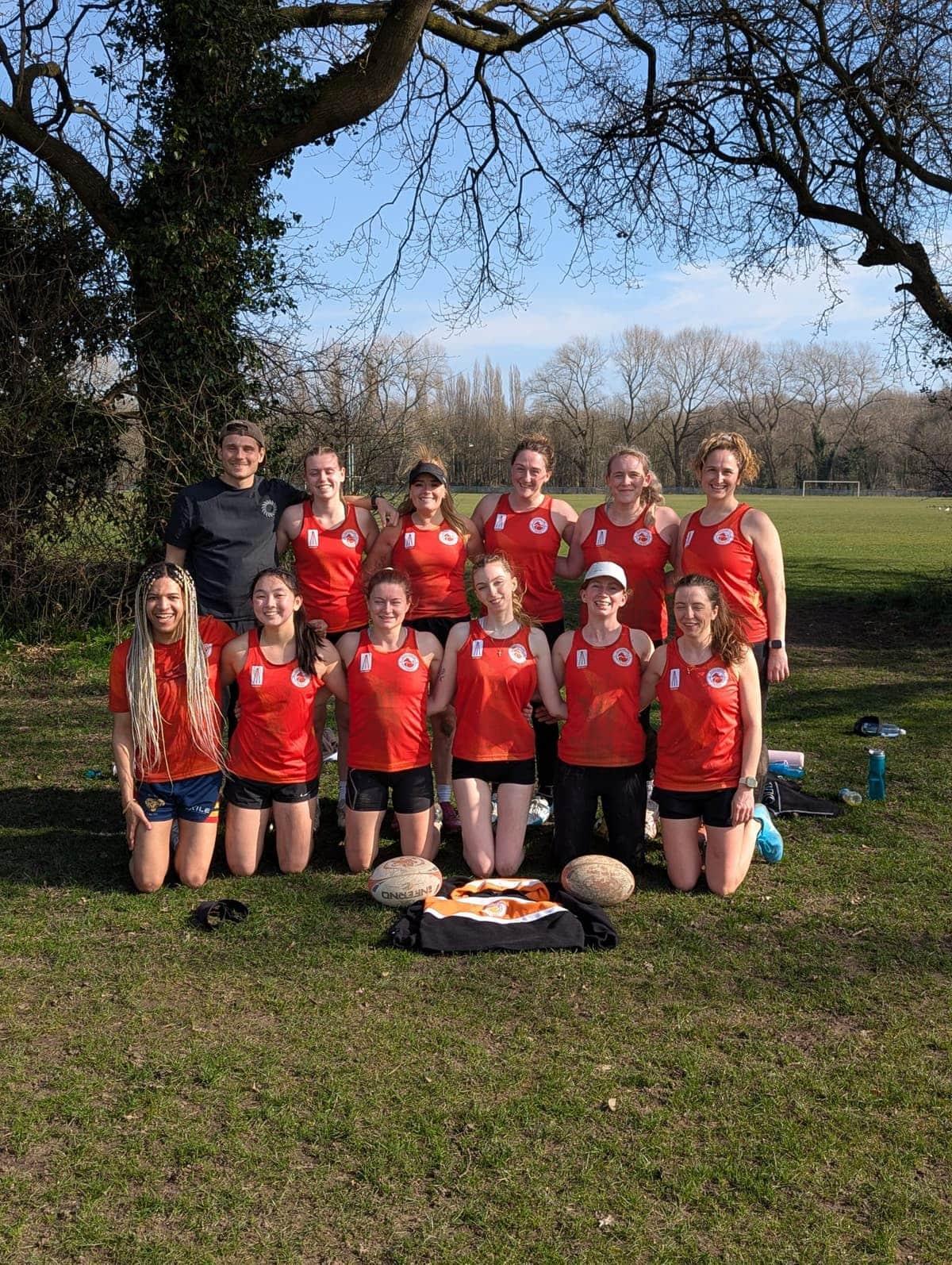 The Manchester Foxes women's touch rugby squad together on a grass pitch with match balls before a game